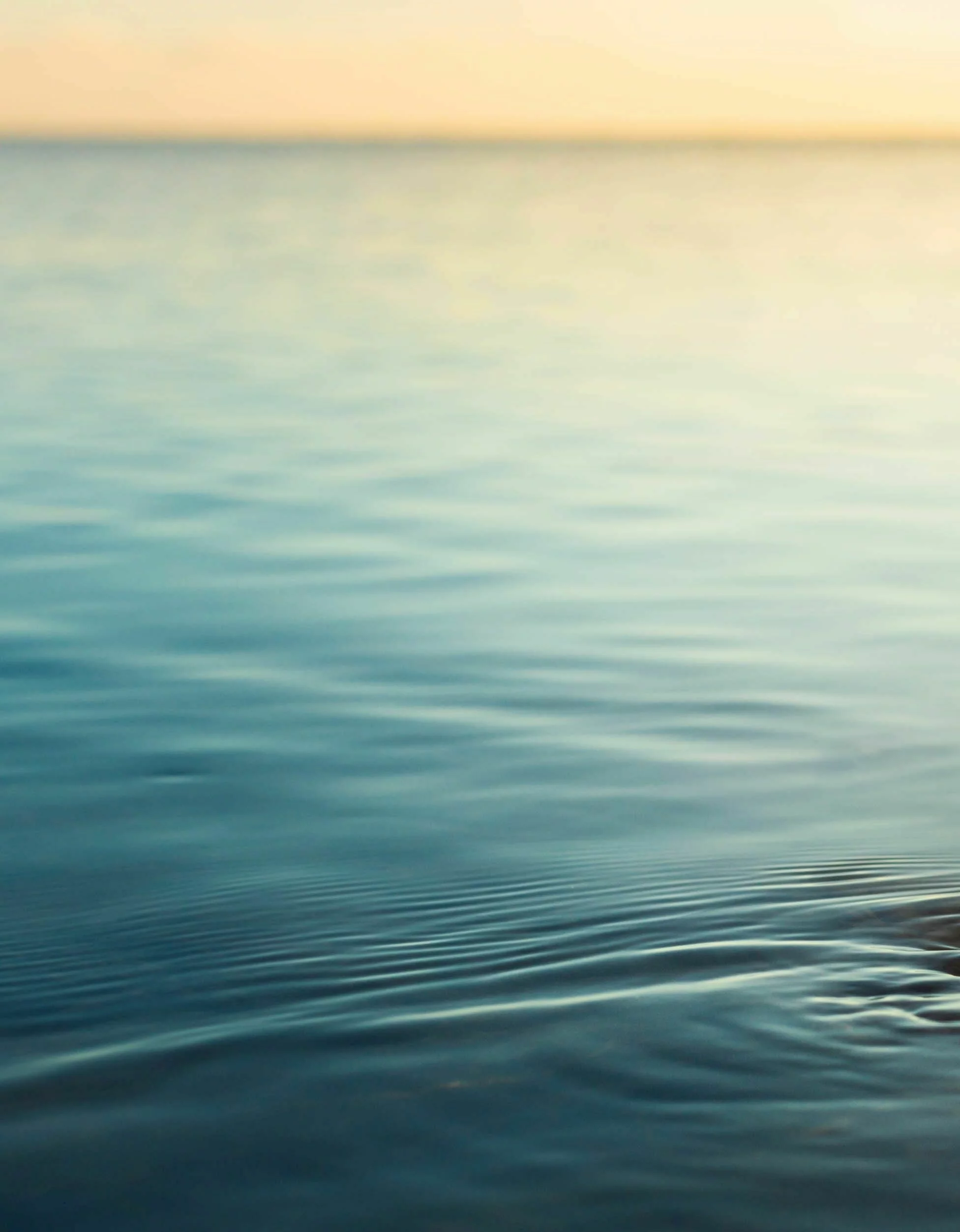 Menschenhand taucht in ruhiges Meerwasser bei Sonnenuntergang.